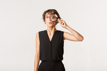 Funny girl looking through magnifying glass with amazed face, standing over white background