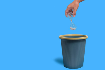 Hourglass is thrown into trash, blue background.Concept of time loss, elapsed time.