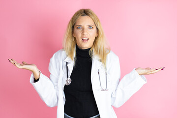 Young blonde doctor woman wearing stethoscope standing over isolated pink background clueless and...
