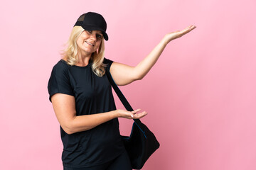 Middle age woman with sport bag isolated on pink background extending hands to the side for inviting to come