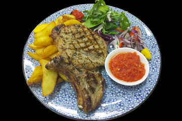 grilled pork bones and potato wedges in a blue plate on a black background, next to the meat parsley and tomato sauce