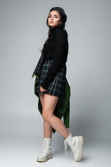 full length of young woman in green leather jacket, checkered skirt and black beret posing on grey - obrazy, fototapety, plakaty