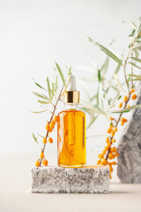 Essential oil and  branch of sea-buckthorn with berries and leaves on stone podium. Natural cosmetic