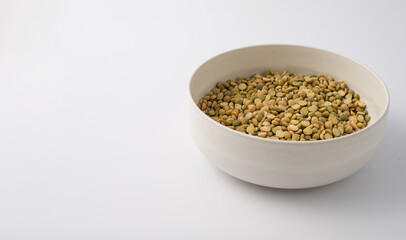 White round plate full of uncooked green lentils. isolated on white