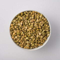 Green lentils on white round pot isolated. top view
