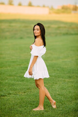 Young woman walks barefoot in meadow on sunny day.