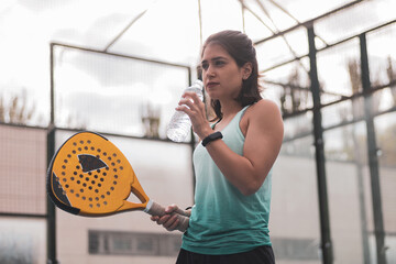 a girl padel player drinking water between the break of the match. - obrazy, fototapety, plakaty