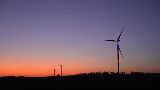 Three wind generators in the evening twilight. The blades of the generator in the foreground are illuminated and rotated.