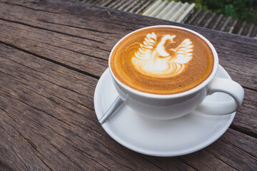 The top view of the white beautiful cup of hot coffee which have latte art as a swan on the surface of the latte on the wooden table with copy space