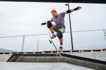 Agile mature skater in a watch cap doing tricks with a skateboard at skate park © zzzdim