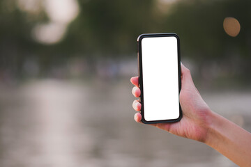 Mock up image of hand holding mobile phone with blank white screen and blur background in the garden with copy space