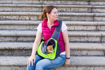 Yaroslavl. Russia. September 20, 2020. An adorable 40-year-old woman sits on concrete steps with a dog in a portable pet bag.