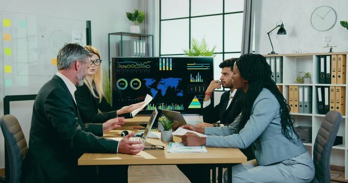 Boardroom of good-looking confident smart professional mixed race team of ecologists which sitting around workdesk and discussing ecological earth problems