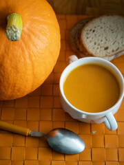 Homemade pumpkin soup in a white cup with bread on napkin on orange wooden rustic background with copy space