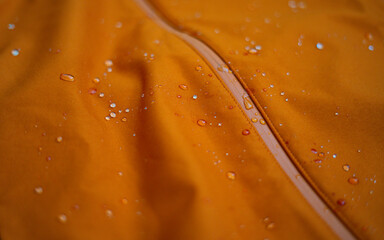 Water drops on a waterproof fabric for mountain clothes. Detail photo of orange wateproof jacket...