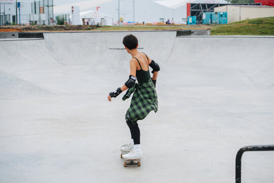 Back image of a woman skater with short hair riding on her board on concrete