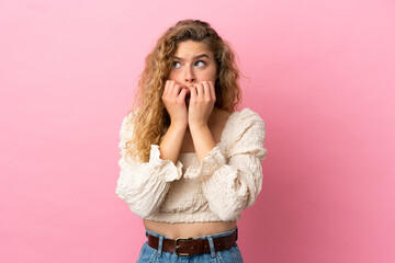 Young blonde woman isolated on pink background nervous and scared putting hands to mouth