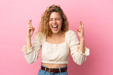 Young blonde woman isolated on pink background with fingers crossing