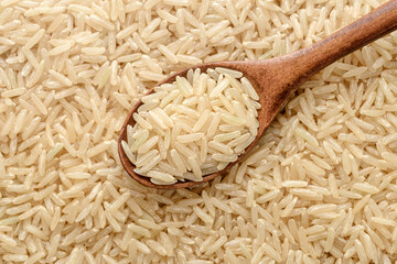 food background of uncooked long brown rice in the wooden spoon, top view