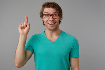 Indoor shot of young positive smiling male, point with a finger upwards and feels happy, isolated...