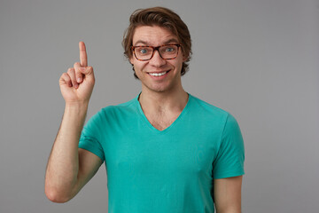 Indoor shot of young positive smiling male, point with a finger upwards and feels happy, isolated over pink background