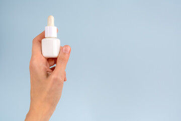 woman hand holding white cosmetic or medicine bottle with pipette on blue background with copy space. mockup of cosmetic or medicine bottle