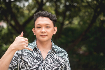 A young teenage male reminding to call him. Gesturing with his hands. Outdoor park scene.