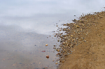 still lake water sandy beach with pebbles with copy space 