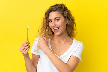 Young caucasian woman holding a brushing teeth isolated on yellow background celebrating a victory