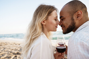 Portrait of a young couple sitting on the beach and drinking wine