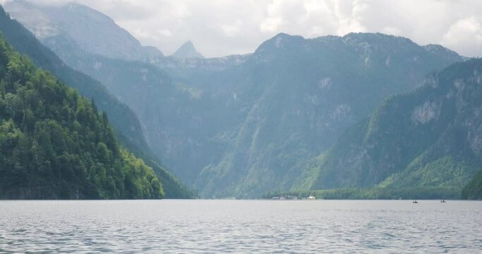Konigssee lake in Bavaria, Germany on a hazy Summer day, with surrounding mountains covered in green. Static shot, audio, landmark, popular, touristic.