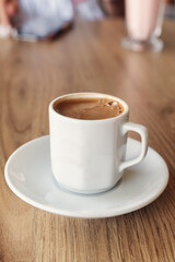 Traditional Turkish coffee in small white cup on wooden table. Selective focus. Vertical photo