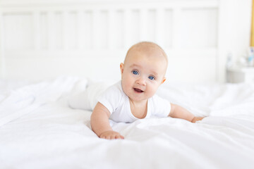 Portrait of cute and smiling four month old baby girl playing on the bed in her room. Happy and dry kid. 