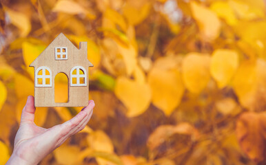 The symbol of the house in the girl's hand on the background of yellow leaves
