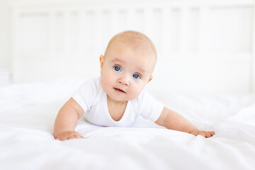 Portrait of cute and smiling four month old baby girl playing on the bed in her room. Happy and dry kid. 