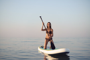 Young attractive woman standing on paddle board - obrazy, fototapety, plakaty