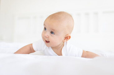 Portrait of cute and smiling four month old baby girl playing on the bed in her room. Happy and dry kid. 