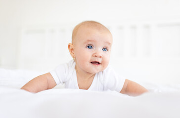 Portrait of cute and smiling four month old baby girl playing on the bed in her room. Happy and dry kid. 
