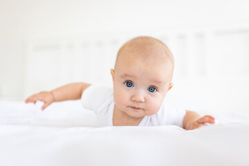 Portrait of cute and smiling four month old baby girl playing on the bed in her room. Happy and dry kid. 