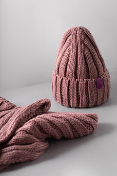Small red knitted hat with on a white scarf jn grey background. woolly hat Closeup.
