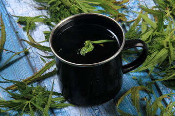 Marijuana herbal tea in a cups and green cannabis leaves around. Blue painted wooden board background. Hemp Tea. Cannabis herbal tea 