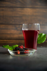 fresh mulberry in bowl and juice in glass on dark background.