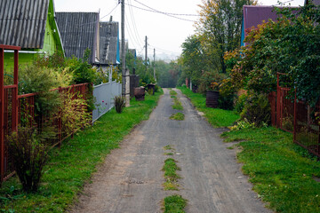 Dirt road in village with private houses goes into distance along high fences. Private sector, single storey building, rural life outside city.