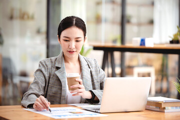 Asian businesswoman working on computer and drinking coffee at the office