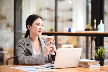 Asian businesswoman working on computer and drinking coffee at the office