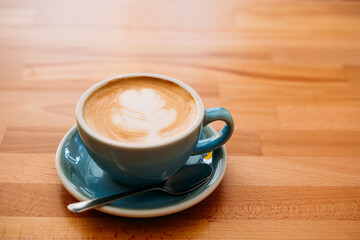 Cup of cappuccino with latte art. Coffee in blue cup on wooden table in cafe. Concept of easy breakfast. Top view, big mug