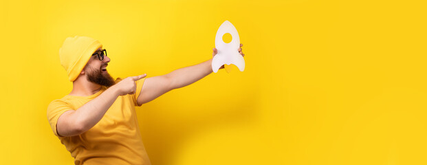 man pointing at rocket over yellow background, concept of startup, panoramic image