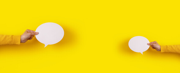 two talk bubbles speech icon in hand over yellow background, panoramic layout - obrazy, fototapety, plakaty