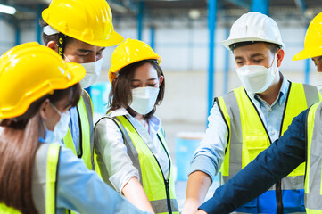 Factory employee of engineers, foreman technicians and staff. Wear a mask hard hat and vest. Standing in a circle, holding hands together Joining forces to create success in the organization. Teamwork