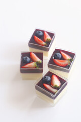 Vanilla Panna Cotta with Berry Compote, in square shot glasses, on a white background.